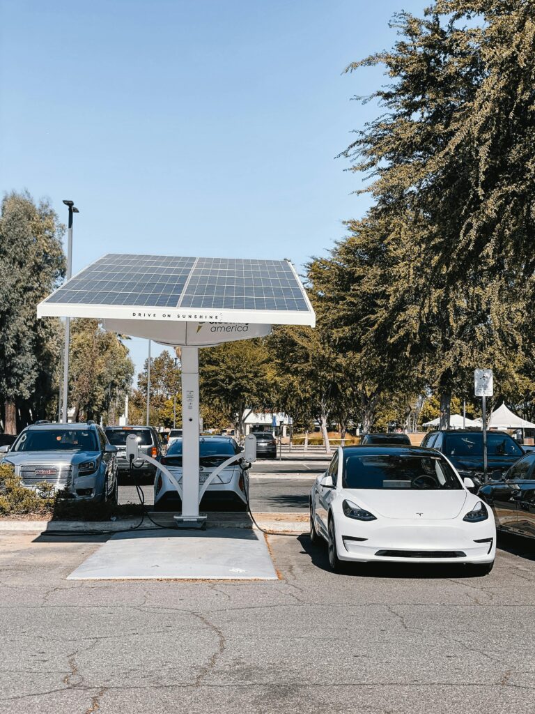 pexels-photo-9800033-9800033 A white electric car charging under a solar panel in an urban setting, showcasing renewable energy use.